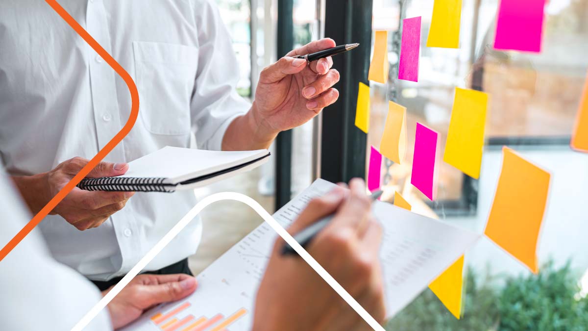 Two people reviewing sticky notes on glass wall.